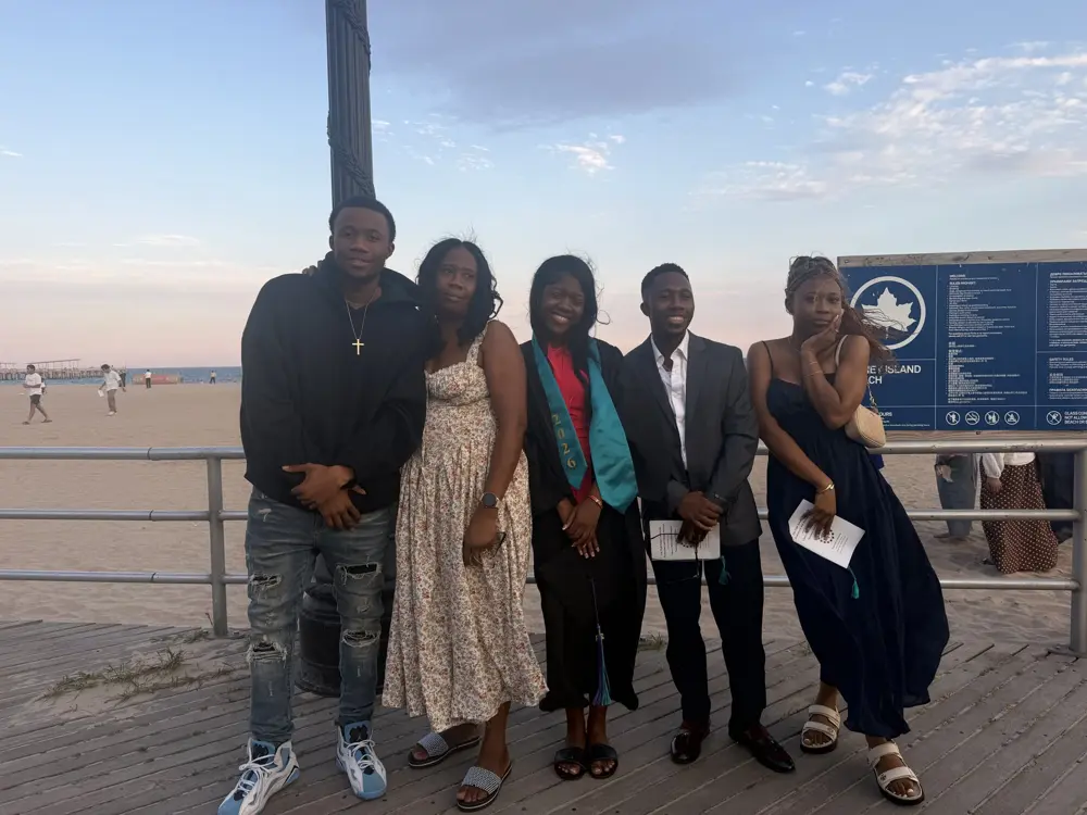 Rose wearing her graduation stole, standing with family on the Coney Island boardwalk at sunset