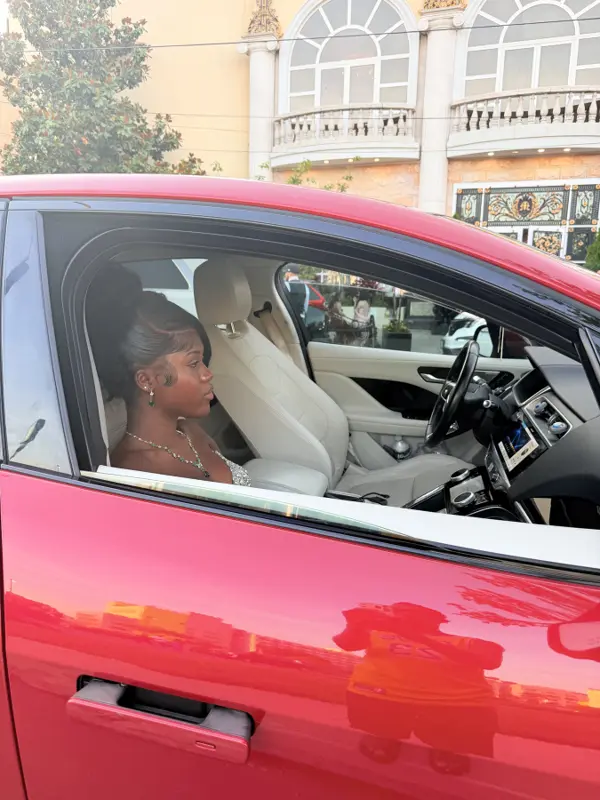 Rose in her prom look seated in the driver's seat of a red car